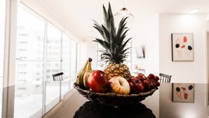 A fruit bowl on a table with a city view through large windows.