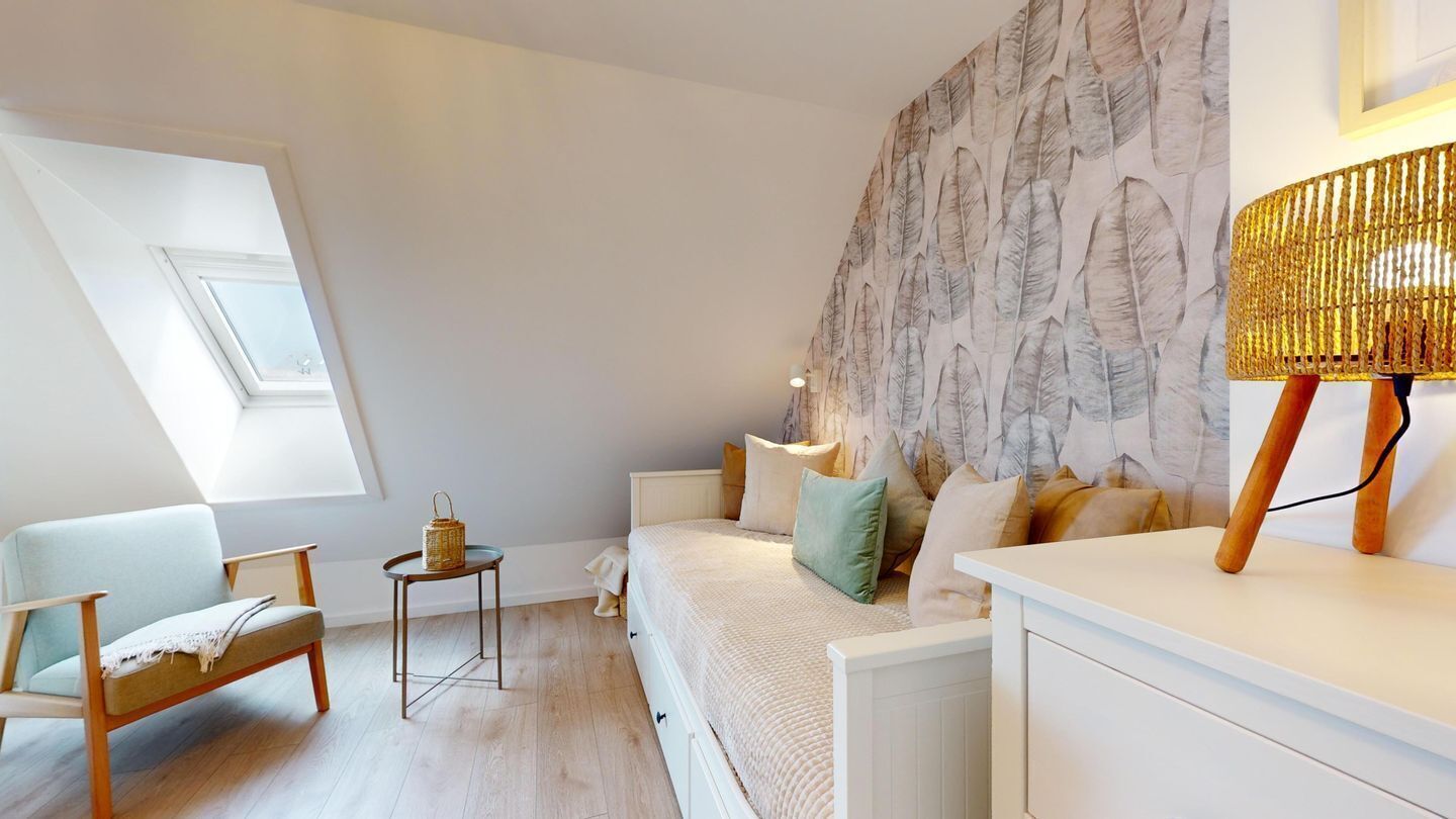Un dormitorio moderno con tragaluz, pared con estampado, sofá, mesita de noche y lámpara.