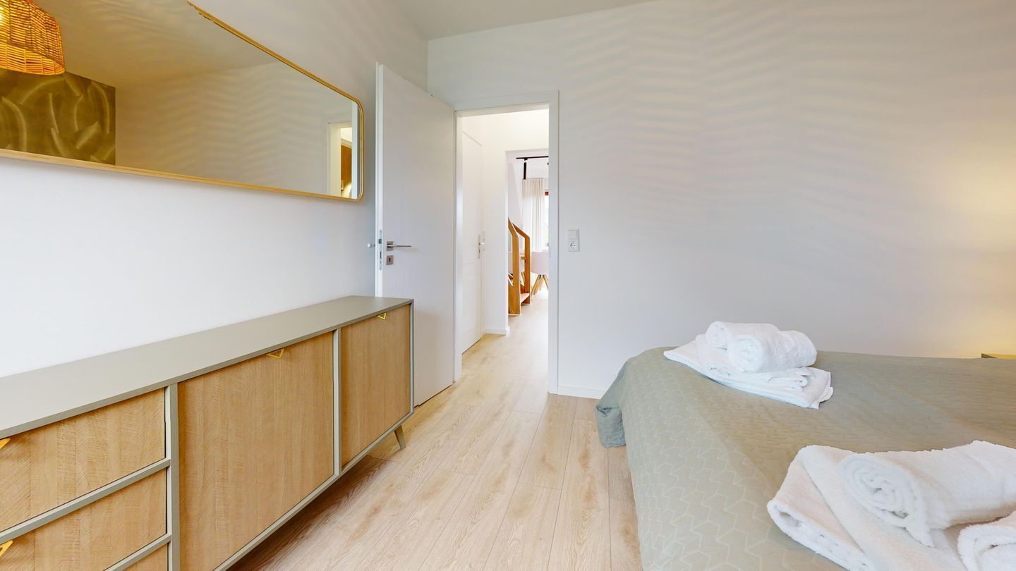 Ein modernes Hotelzimmer mit einem Holzinlay und einem Bett mit einem grün gemusterten Überwurf, sowie einem großen Spiegel.