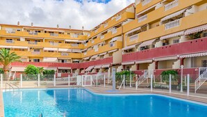 A swimming pool surrounded by a multi-story building with balconies and a red and yellow facade.