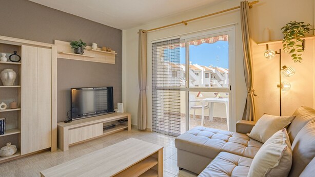 A modern living room with a flat-screen TV, wooden shelving, a beige sofa, and a balcony with a view of buildings.