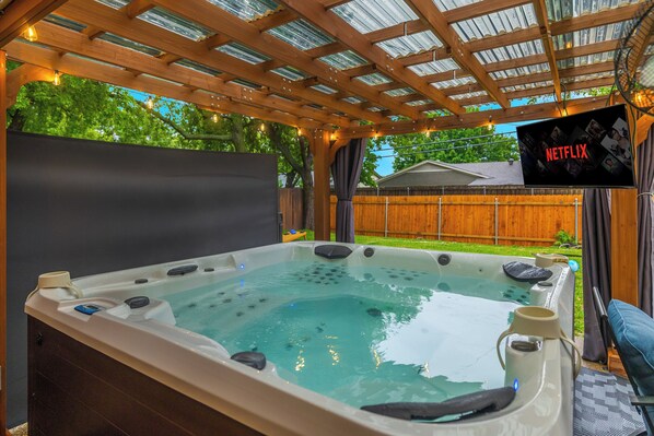 Un bain à remous sous une pergola en bois, avec un écran Netflix installé au-dessus.