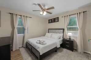 Une chambre à coucher avec un lit, une table de chevet, un ventilateur de plafond et des rideaux.