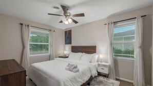 A bedroom with a bed, nightstands, a ceiling fan, and windows with curtains. - 3-Bed Haven - 6 pple Hot tub, King bed, Pool & ping pong table, Grill, Fire pit (Richardson)