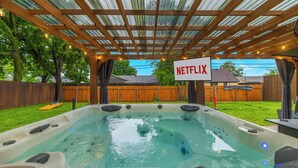 A hot tub with a wooden pergola overhead and a sign that reads "NETFLIX". - 3-Bed Haven - 6 pple Hot tub, King bed, Pool & ping pong table, Grill, Fire pit (Richardson)
