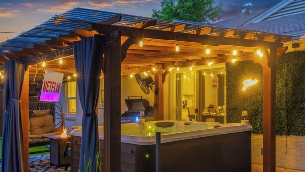 A hot tub under a wooden pergola with string lights, a Netflix sign, and a neon sign. - 3-Bed Haven - 6 pple Hot tub, King bed, Pool & ping pong table, Grill, Fire pit (Richardson)