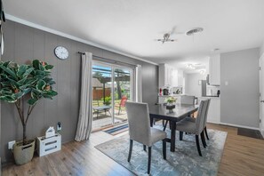 Une cuisine moderne avec des meubles blancs, un coin repas doté d’une table et de chaises en bois foncé, et une grande fenêtre agrémentée de rideaux.