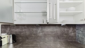 Een moderne keuken met een grijs aanrecht, witte kastjes en een roestvrijstalen waterkoker.