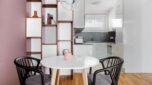 Een moderne keuken met witte kasten, een ronde eettafel met twee stoelen en een hanglamp boven de tafel.