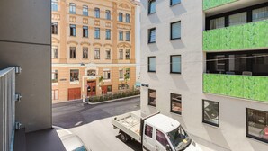 Uitzicht op een straat met een witte vrachtwagen langs de kant, een geel gebouw met meerdere ramen, en een modern gebouw met een groene gevel.