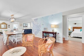 Una habitación amplia con comedor, sillas de mimbre, una mesa de madera, un mural de mapa y una cama con cabecera blanca.