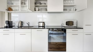 Una cocina moderna con armarios blancos, encimera negra, cafetera, hervidor, microondas y lavavajillas.
