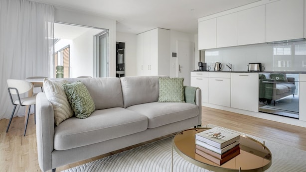 Una sala de estar moderna con un sofá, una mesa de centro y una cocina con armarios y electrodomésticos.