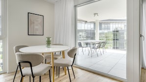 Un comedor moderno con una mesa redonda y cuatro sillas, una obra de arte abstracta enmarcada en la pared y vistas a un balcón con puerta de cristal.