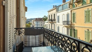 A balcony with wicker furniture and patterned cushions, overlooking a row of buildings with green shutters and balconies. - Upstays Banane Center 80m² Apartment (Cannes)