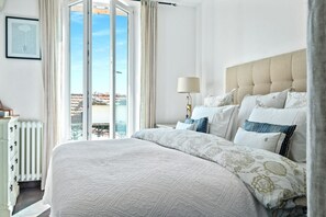 Une chambre avec un grand lit, une table de chevet avec une lampe et une vue sur l’extérieur.