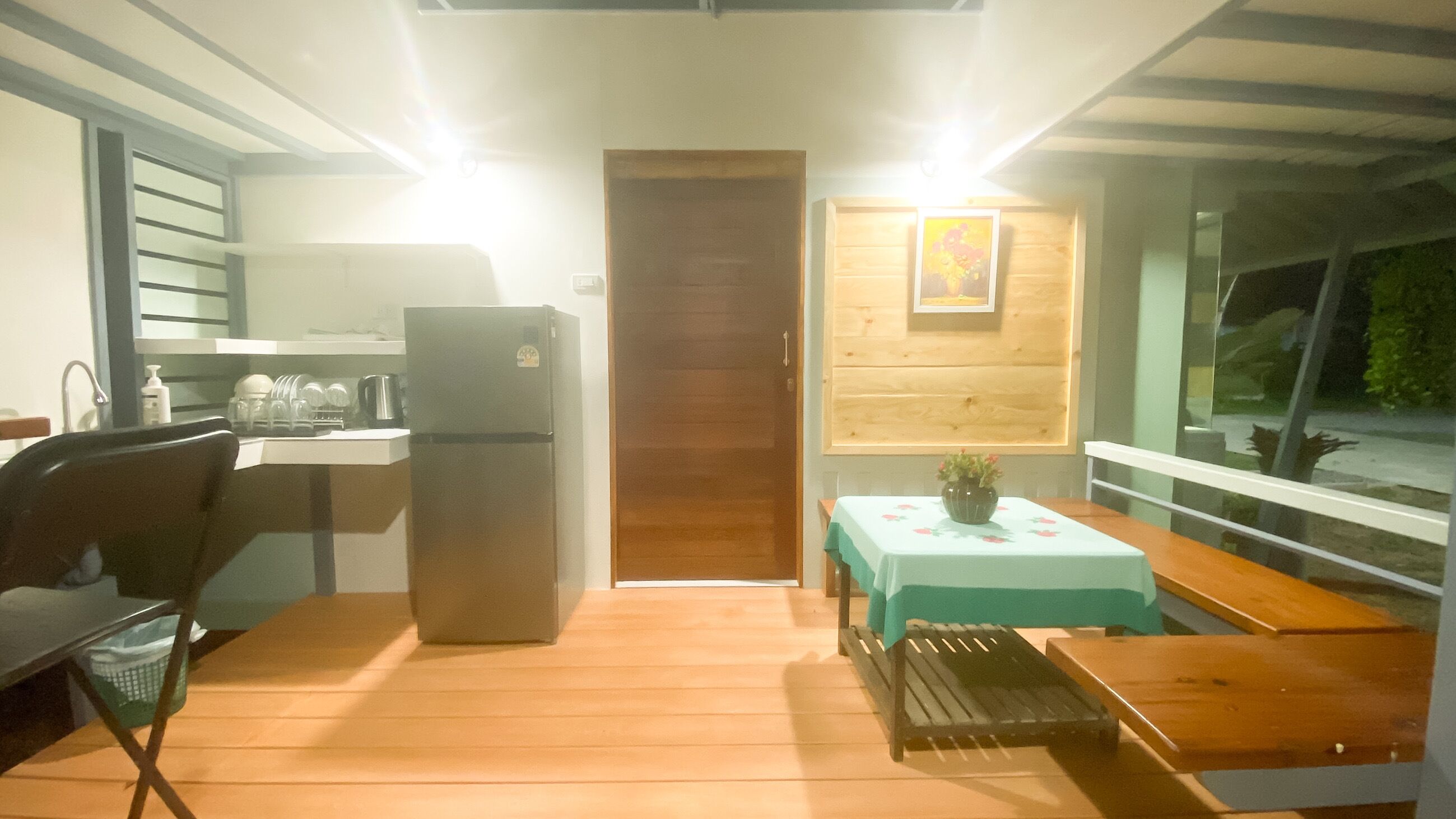 Una cocina compacta con refrigerador, lavamanos y armarios de madera. Hay un comedor con mesa y sillas, y una ventana con vistas.