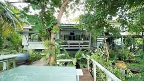 A lush garden with a wooden deck, a covered seating area, and a building with a tiled roof.