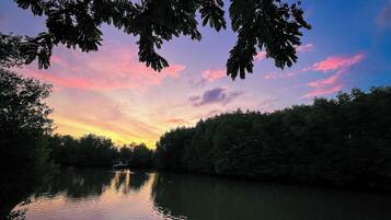 Ein ruhiger Fluss mit einem Boot, umgeben von dichter Baumgruppe und einem farbenprächtigen Himmel.