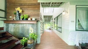 A corridor with wooden flooring, a wooden bench, and a variety of potted plants. - Rimsira (Pathio)