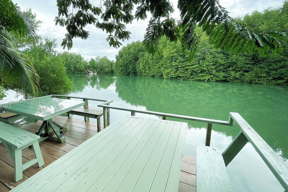 A wooden deck with picnic tables overlooking a calm river, surrounded by lush greenery.