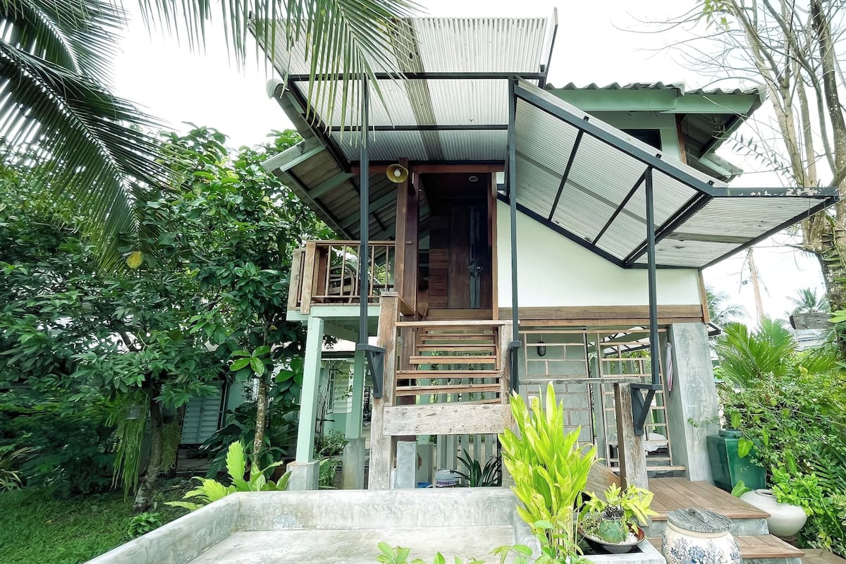 A multi-level house with a wooden staircase, a balcony, and a covered porch area.