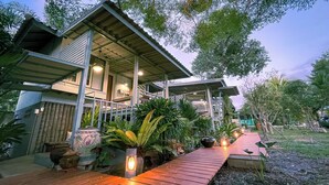 A modern house with a covered porch, potted plants, and a wooden deck. - Rimsira (Pathio)