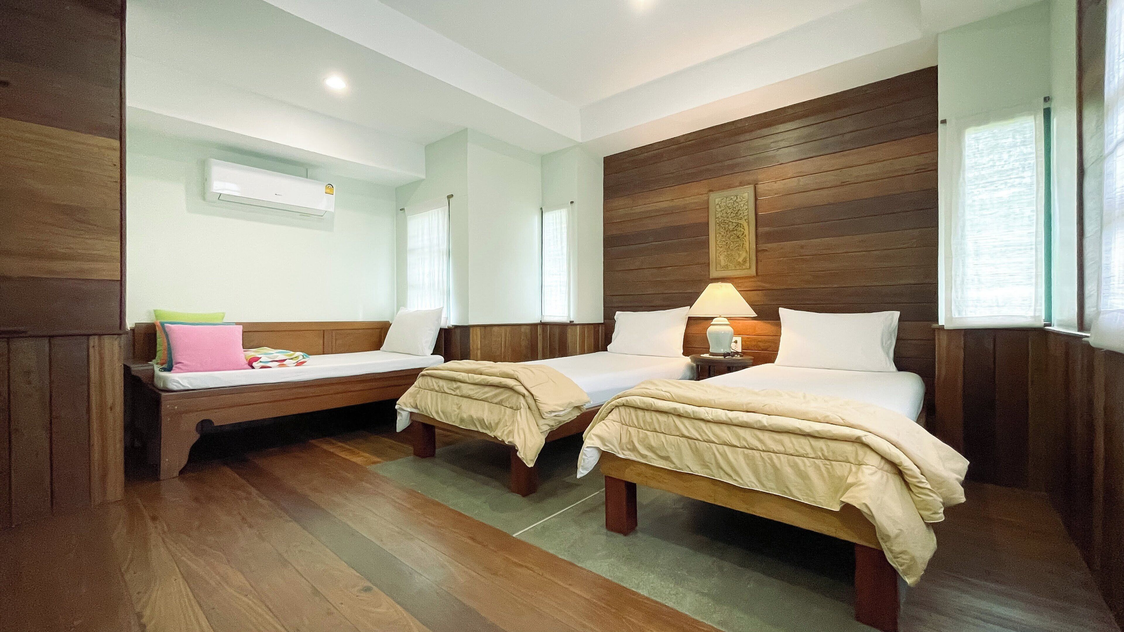 Una habitación con dos camas individuales, paneles de madera en las paredes, un ventilador de techo y una ventana con cortinas.