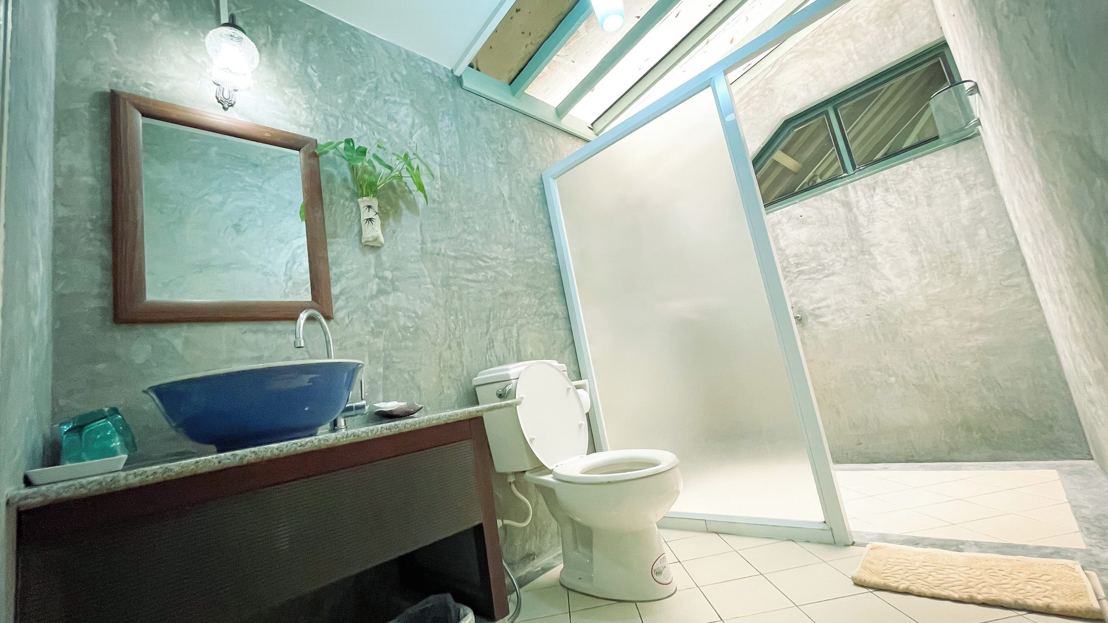 Un baño con lavamanos azul, inodoro, espejo y zona de ducha.