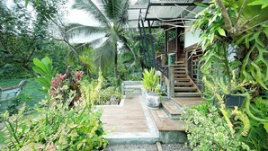 A wooden staircase leading to a covered area surrounded by lush greenery and a boat docked nearby. - Rimsira (Pathio)