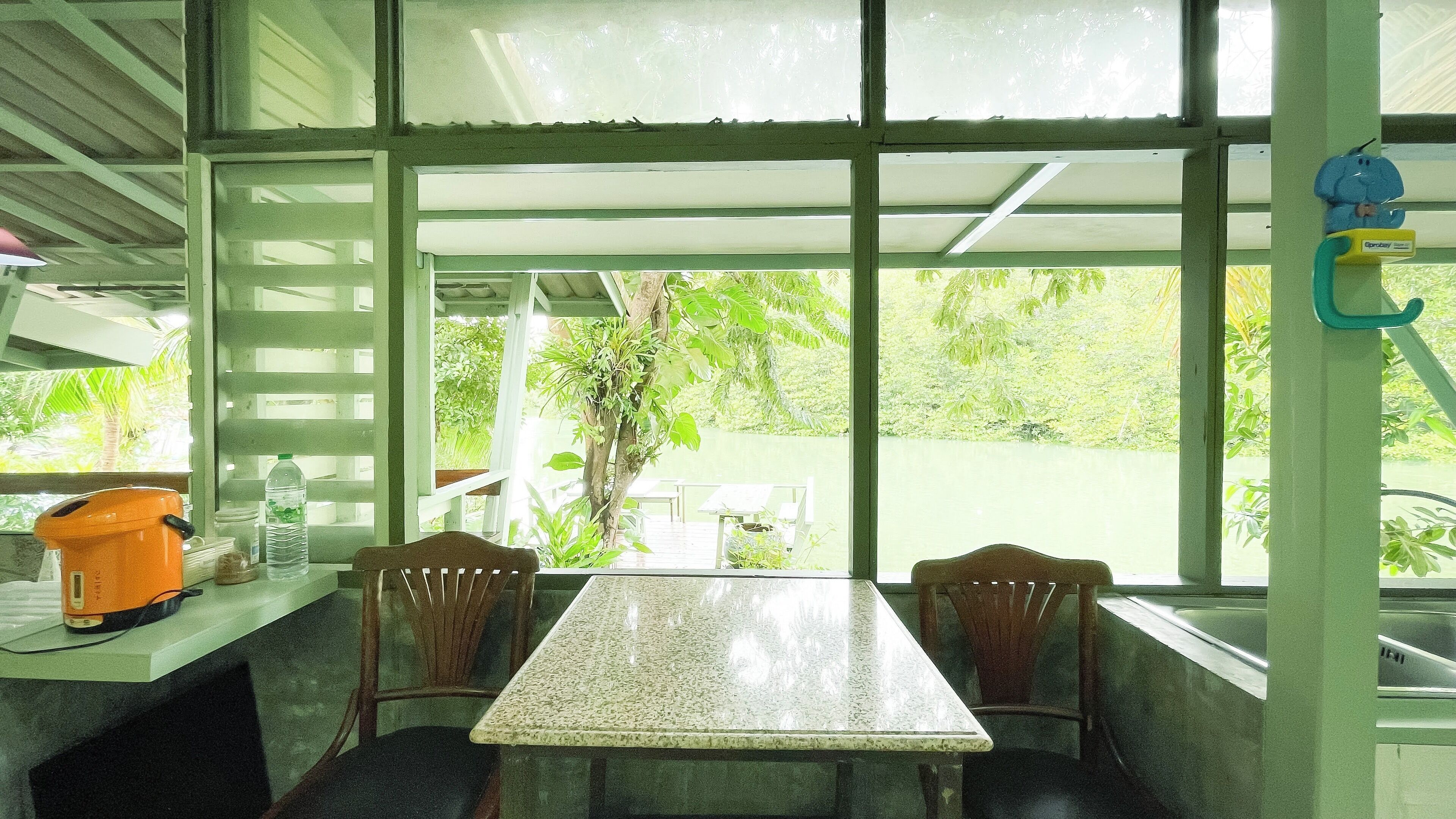 Quarto com mesa e cadeiras, janela com vista para vegetação e um bebedouro no balcão.