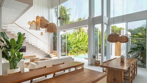 A spacious living area with a wooden dining table, white sofas, and a staircase leading to an upper level. - Villa Belga (Canggu)