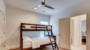 A bedroom with a bunk bed, wooden flooring, a ceiling fan, and a door leading to another room.