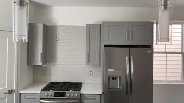 A modern kitchen with stainless steel appliances, grey cabinetry, and a white tiled backsplash.
