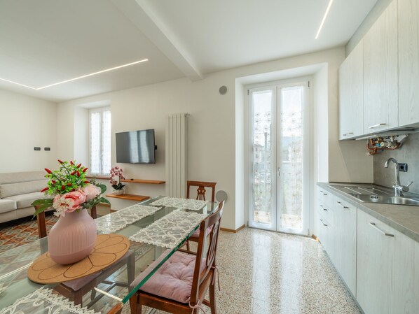 A modern kitchen with a built-in oven, a dining area with a glass table, and a living room with a sofa and TV. - Matilde by Interhome (Luino)