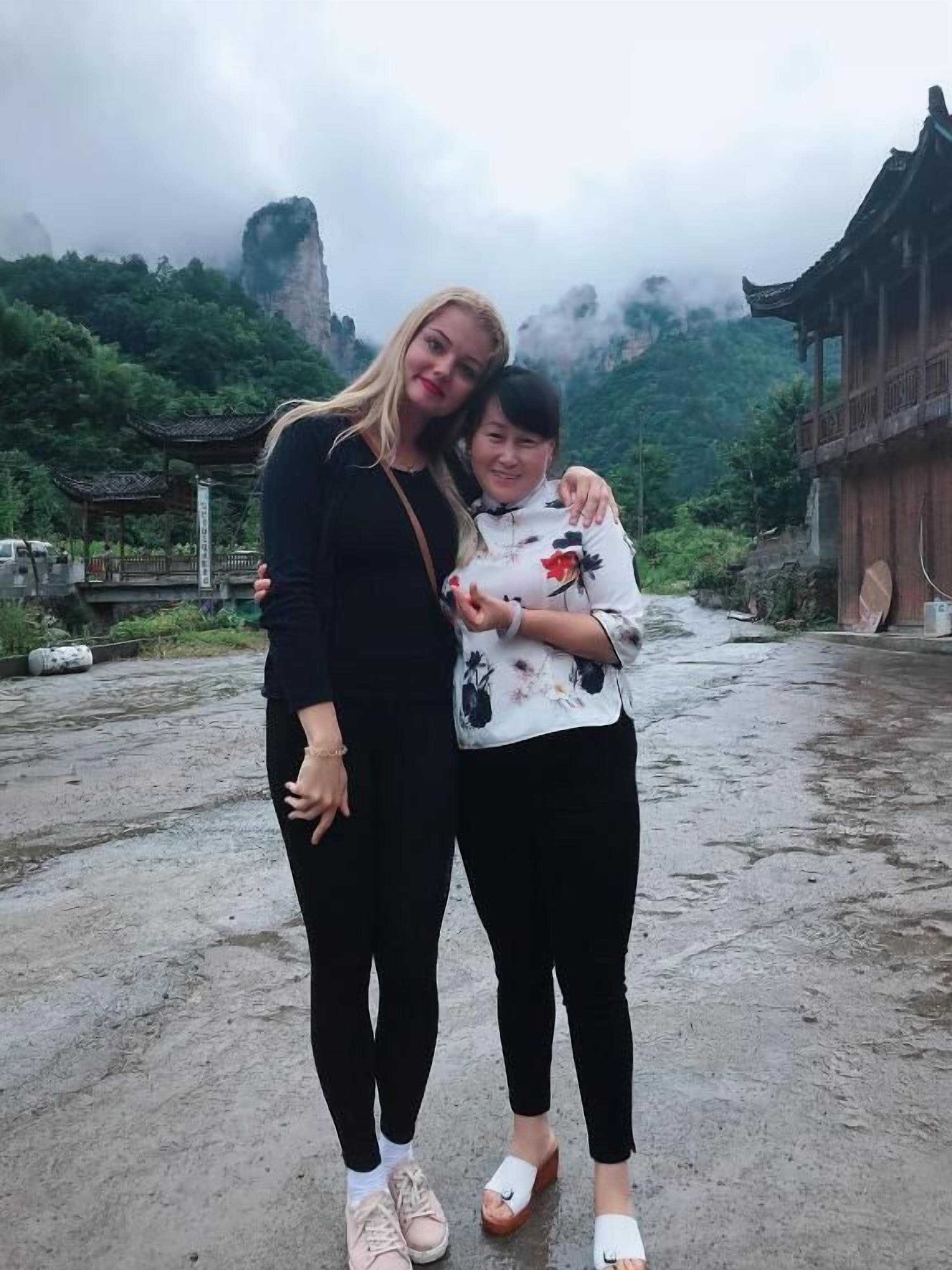 Two people standing in a courtyard with traditional architecture and a mountainous backdrop.