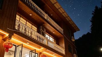 A two-story building with a balcony, outdoor seating, and a view of the night sky.