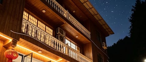A two-story building with a balcony, outdoor seating, and a view of the night sky.