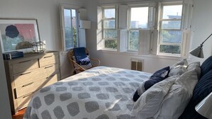 Een slaapkamer met een bed, een stoel, een dressoir en een raam met luiken.