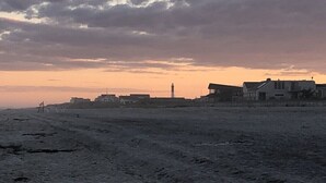 Een strand met een vuurtoren in de verte, zandvlakte en gebouwen langs de kust.