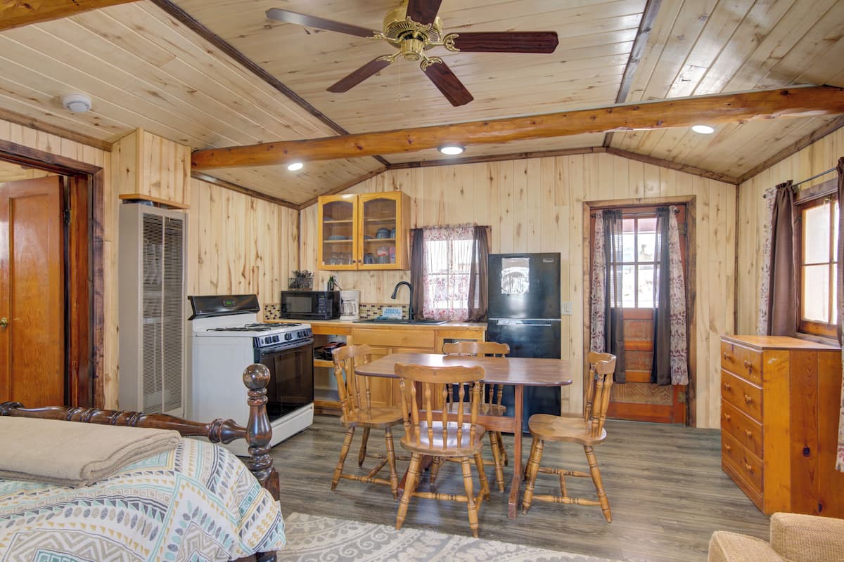 A wooden cabin interior with a kitchen, dining area, and a bed.