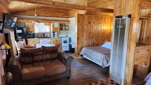A cozy cabin-style room with a sofa, a bed, a small kitchen area, and a television mounted on the wall. - Winmar Cabins (Twin Lakes)