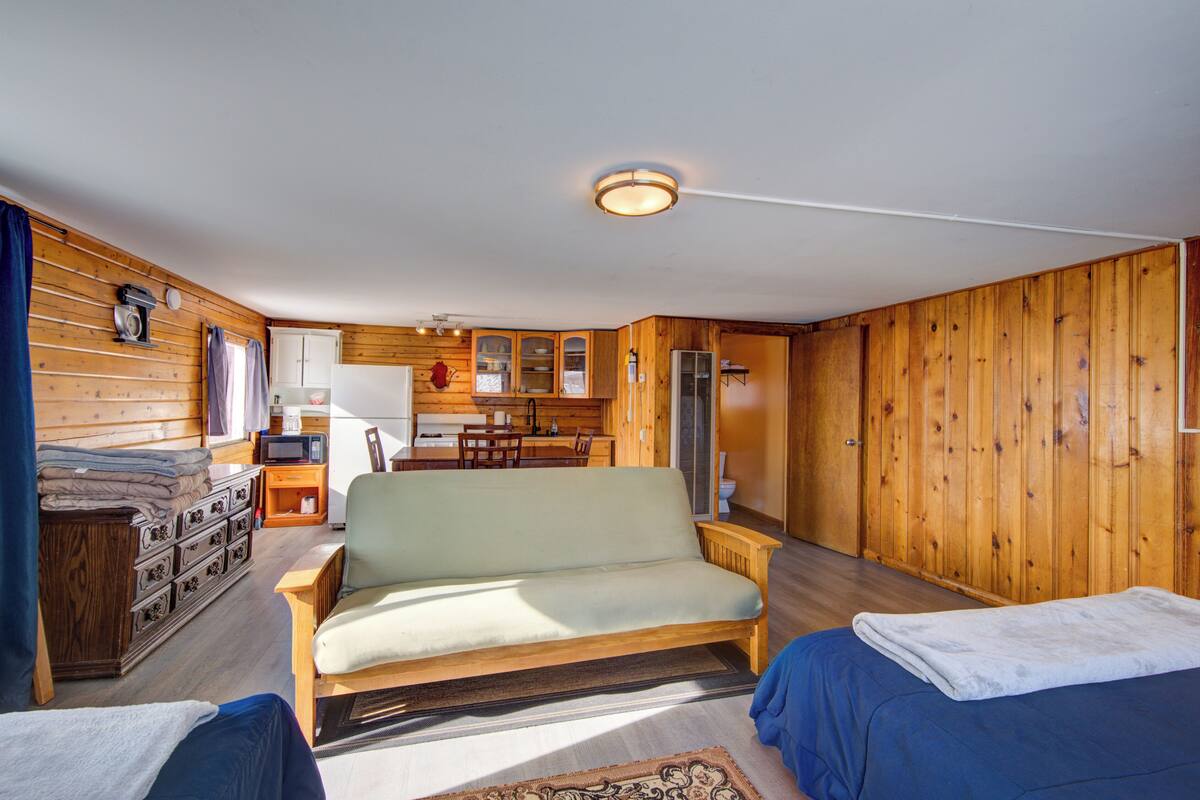 A cozy cabin-style room with a sofa, two beds, a dining area, and wooden walls.