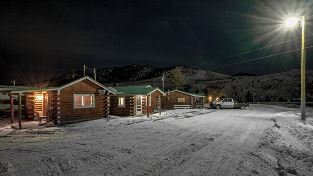 A snow-covered landscape with a row of log cabins, a parked truck, and a bright streetlight. - Winmar Cabins (Twin Lakes)