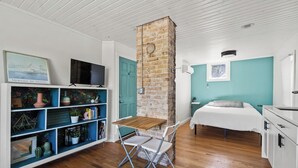 Een knus ingerichte kamer met een bakstenen open haard, een bed, een televisie en een boekenplank met decoratieve objecten.