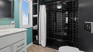 Een badkamer met een douchebekleding van zwarte tegels, een wit toilet en een wit wastafelmeubel met een marmeren blad.