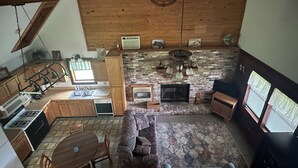 Un vaste espace de vie comprenant un coin salon avec cheminée, une table à manger et une cuisine équipée de meubles en bois et d’une cuisinière à gaz.