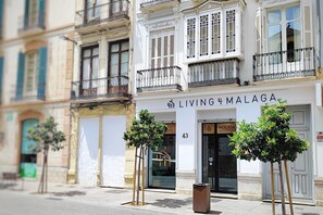 Ein Gebäude mit einem Schild, auf dem "Living4Malaga" steht, und einem Empfangsbereich. Vor dem Eingang befinden sich zwei Bäume.