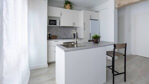 A modern kitchen with white cabinetry, a central island with a sink, a microwave, and a refrigerator. - Aldatseta Home - Apartamento centrico (Bermeo)