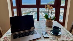 A laptop on a table with a floral tablecloth, a smartphone, a cup, and a potted orchid plant. - Ertzilla apartament - Sea view. (Bermeo)